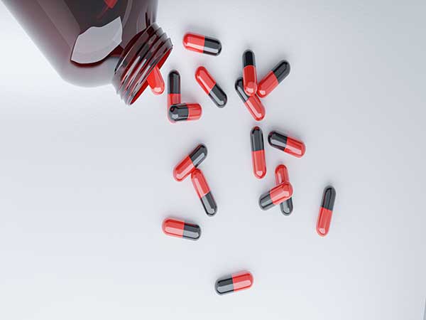 Imagens de frasco com diversos comprimidos em cores vermelho e preto, espalhados sob uma superfície branca.